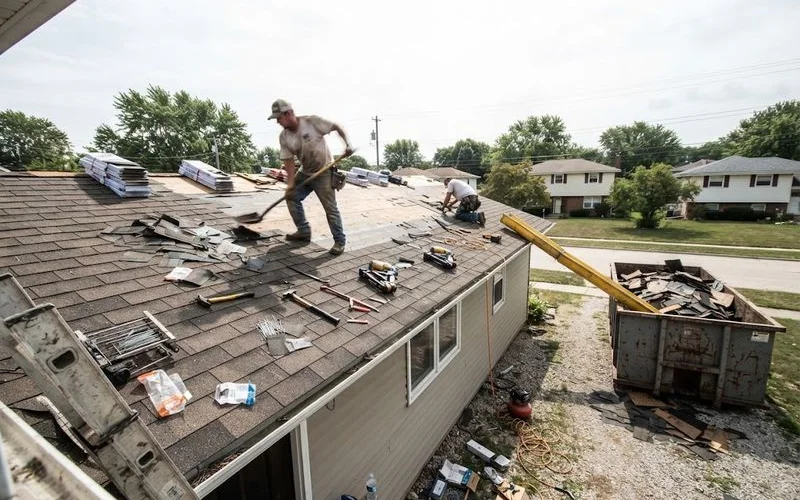 A roofing crew tears off old asphalt shingles and stacks new architectural shingle bundles on a Georgia rooftop during a full replacement